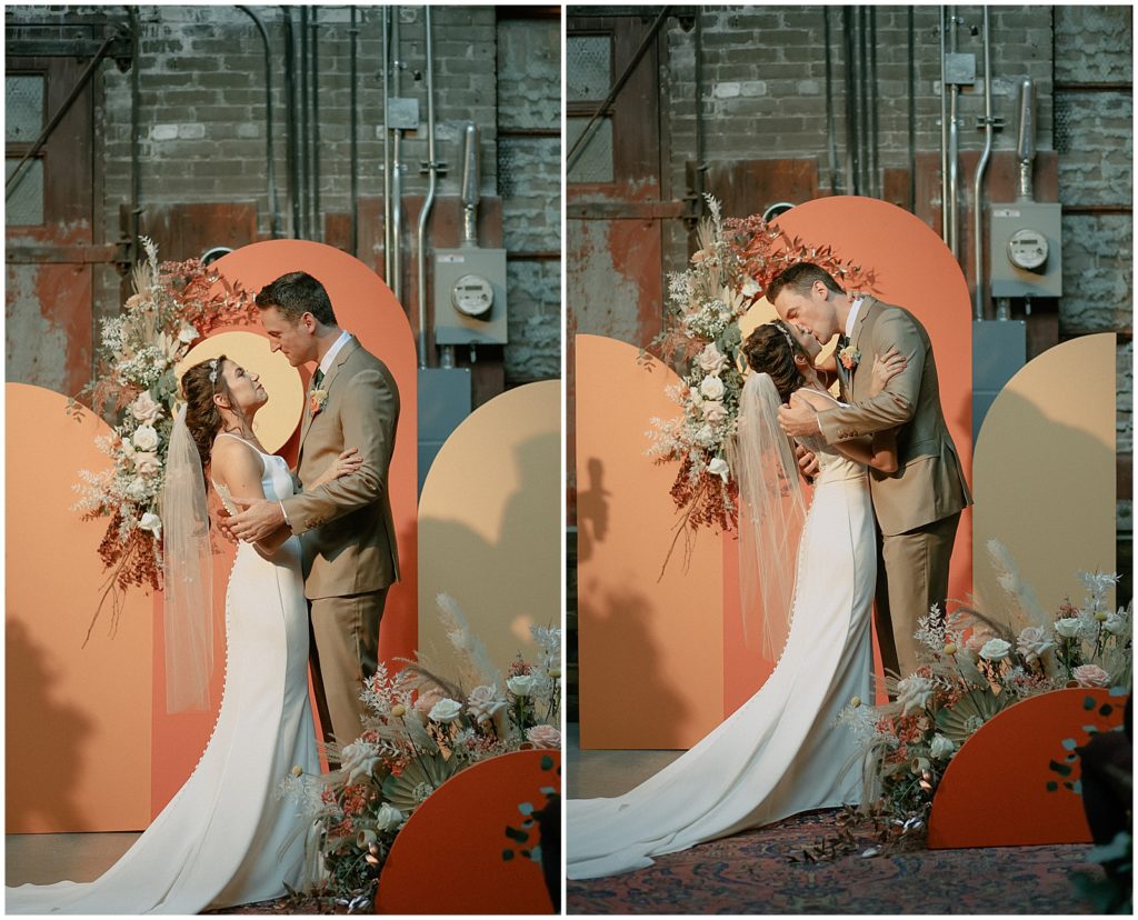 Nora and Steve kiss in front of the orange and yellow ceremony backdrop.