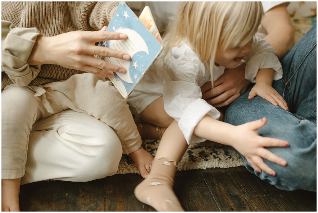 A toddler leans away from her mother who is opening a book.