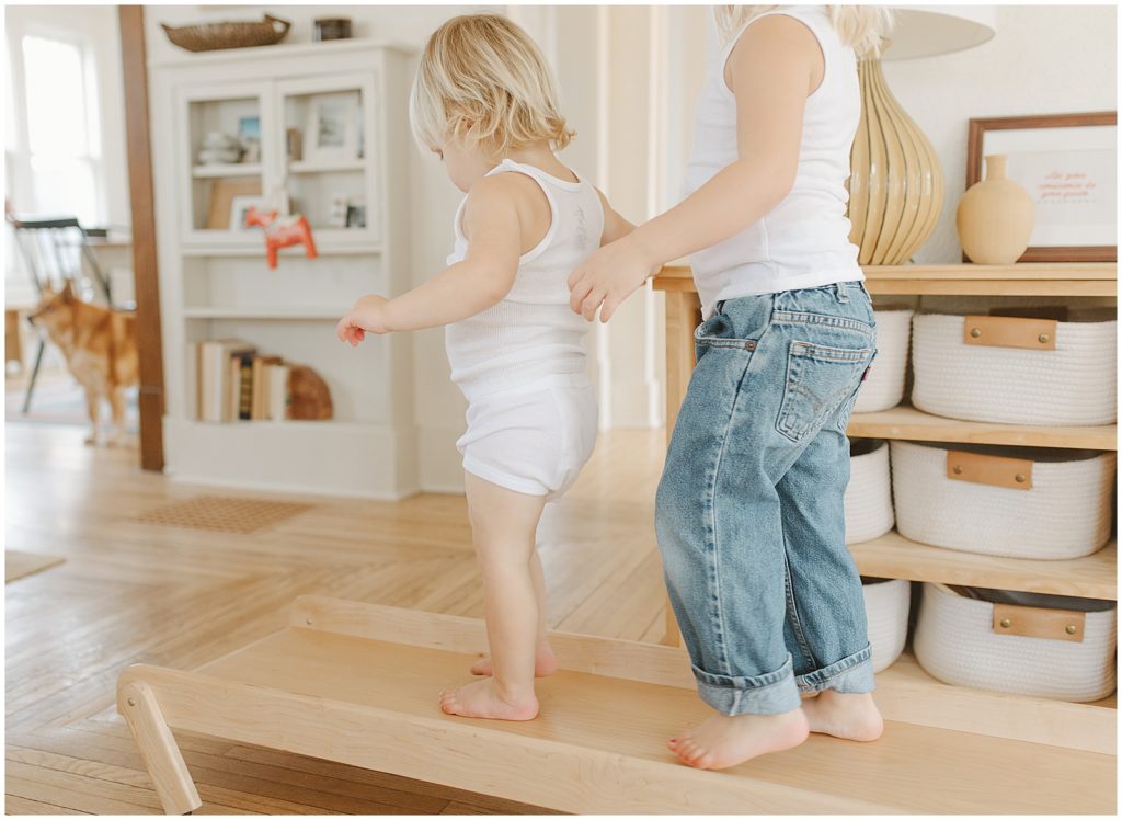 The children walk along a wooden board in their playroom.
