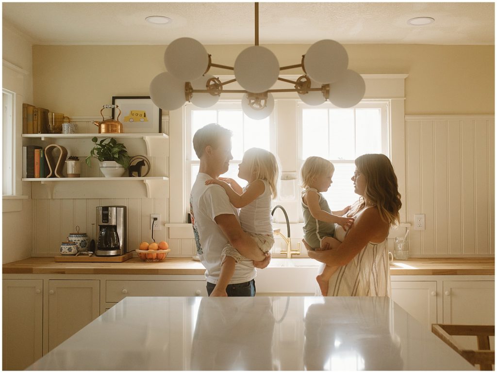 The family stands in the kitchen backlit by the windows over the sink.