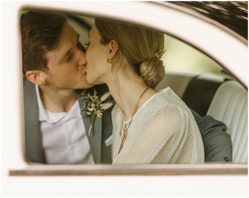 Nick and Sarah kiss in the back seat of a vintage car for their wedding at The Cooperage.