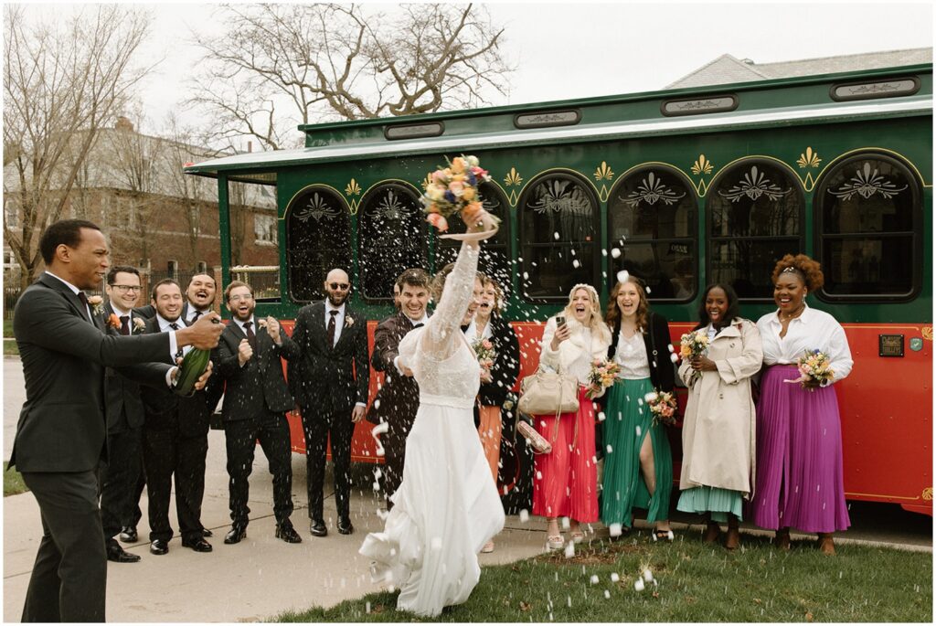 A wedding party sprays champagne on a Milwaukee bride and groom walking too a trolley.