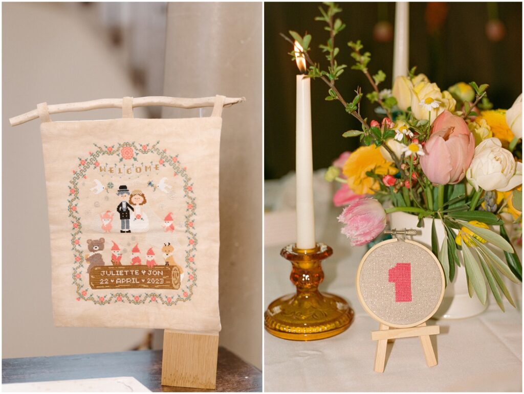 A cross-stitched table number sits beside a bouquet and candlesticks.