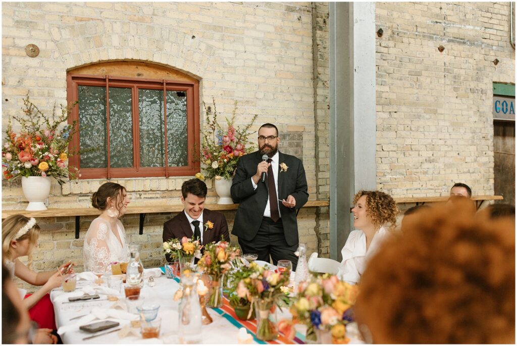 A groomsman gives a speech while guests watch.