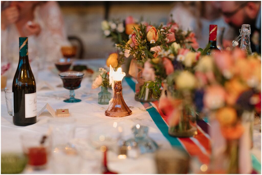 A candle burns low in a glass candleholder on a colorful wedding tablescape.