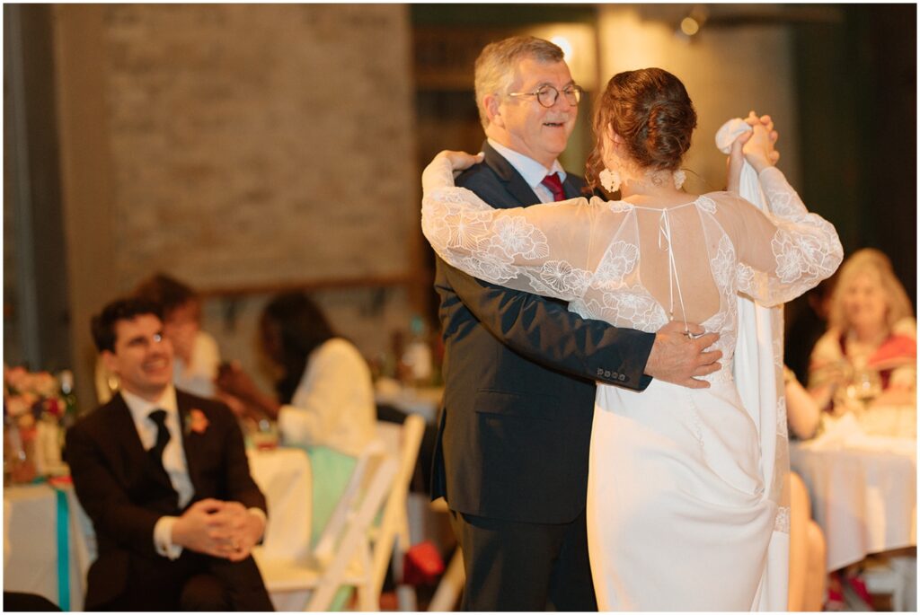 Juliette's father smiles and leads her in a dance.