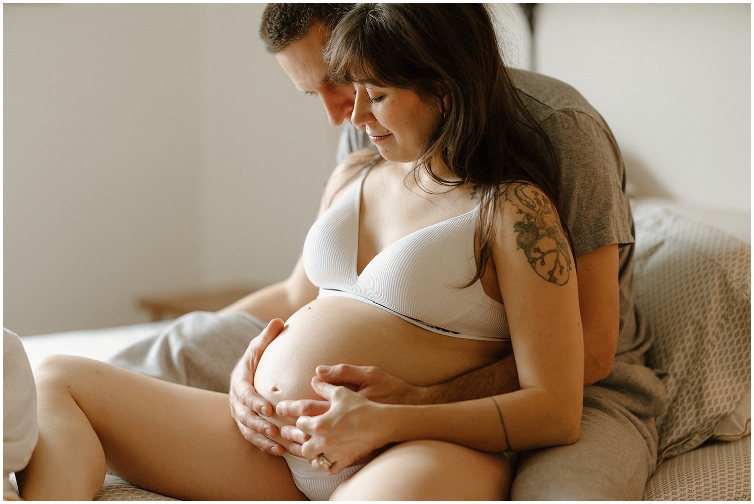 A woman leans against a man in a bed during pregnancy photography session.