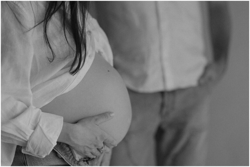 A woman holds her baby bump in black and white pregnancy photography.