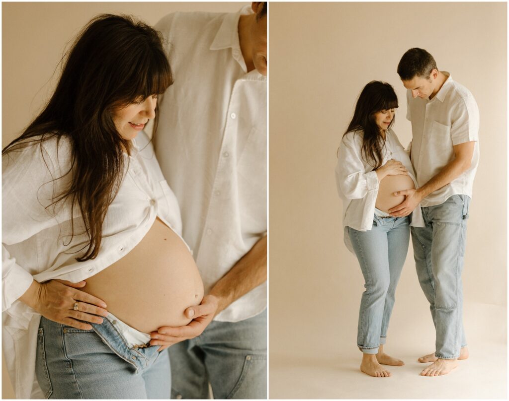 A husband and wife in white shirts smile down at her baby bump.