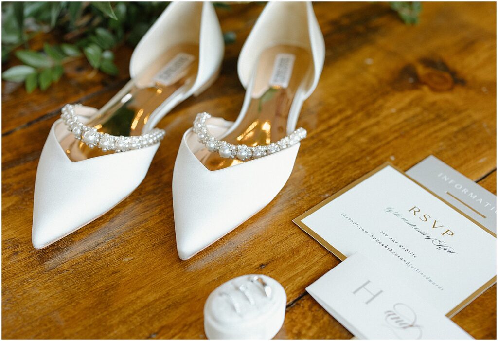 Pearl-lined wedding shoes sit beside an invitation suite.