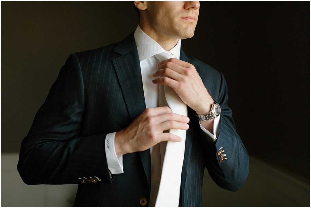 A groom straightens the tie of his wedding suit.