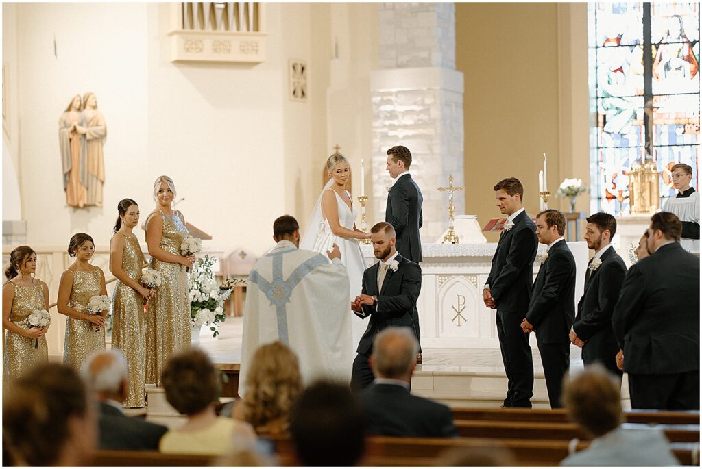 A bride and groom hold hands with their wedding parties standing on either side of them.
