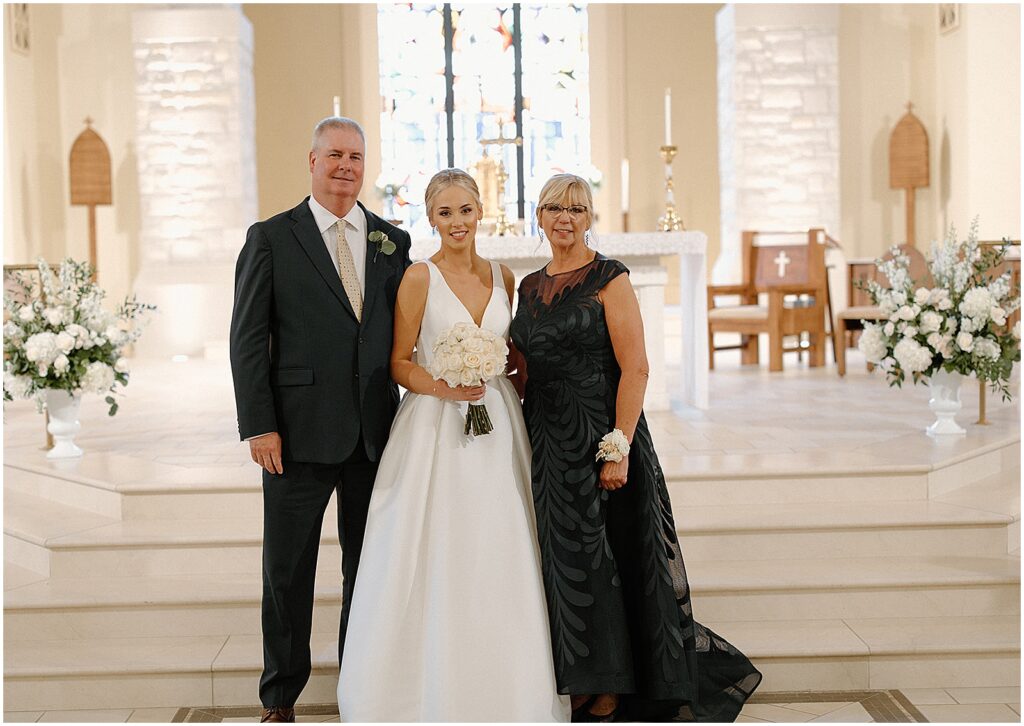 A bride stands between her parents for a formal family photo.