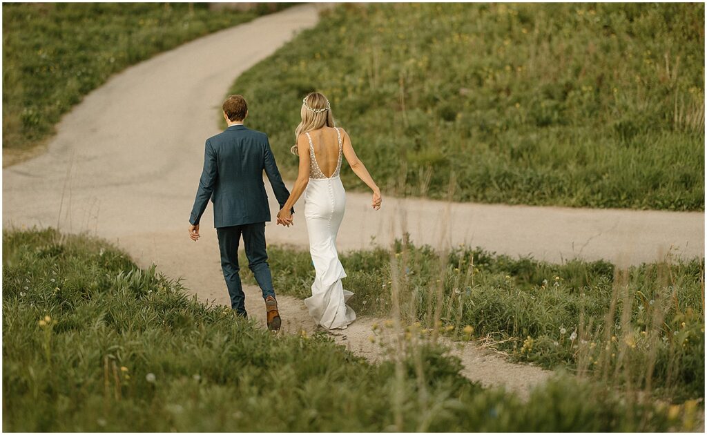 A bride and groom walk down a winding path in a field at Riverside Park.