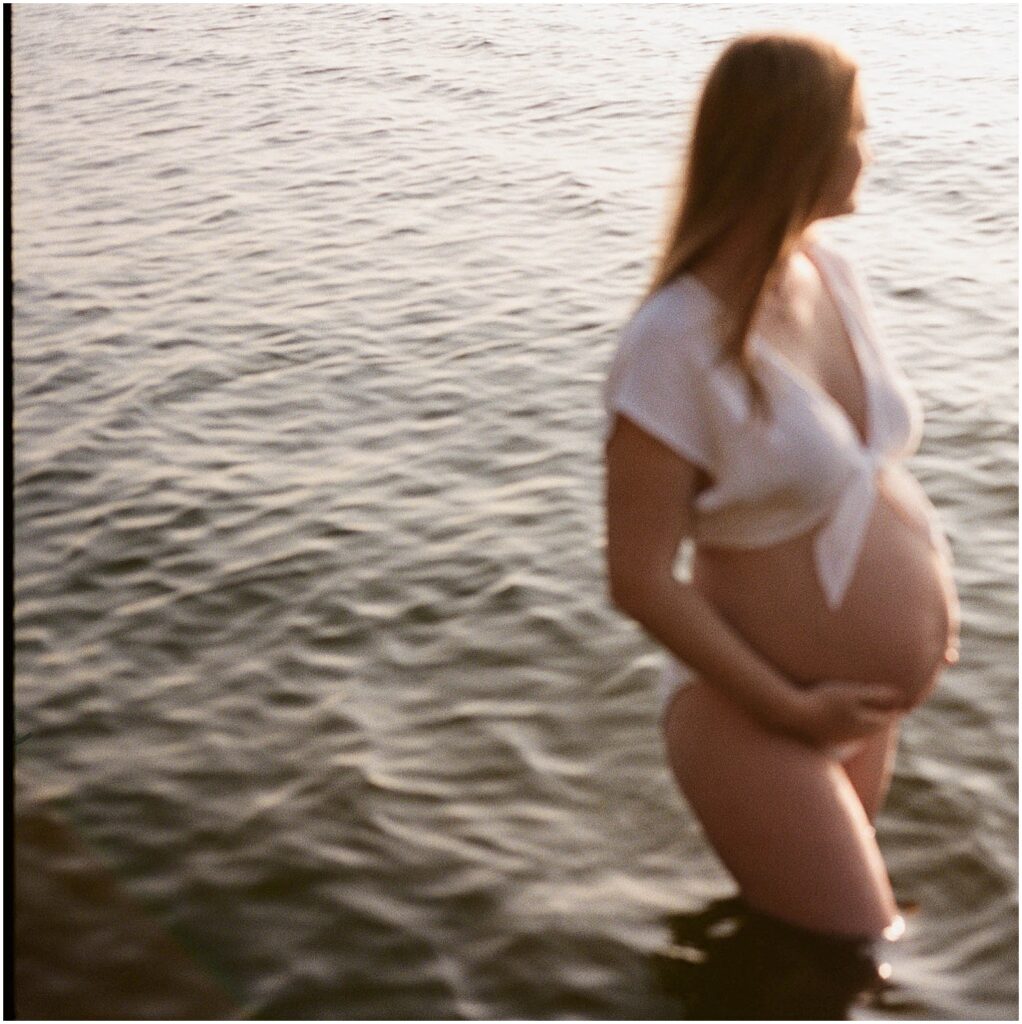A woman poses for a golden hour maternity photo in a Door County lake.