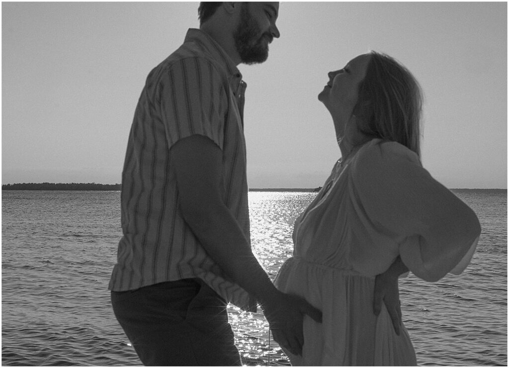A man and woman smile at each other while they pose for Door County maternity photos.