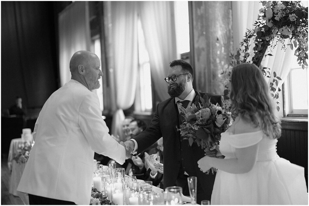 A groom shakes his father-in-law's hand in a candid wedding photo.