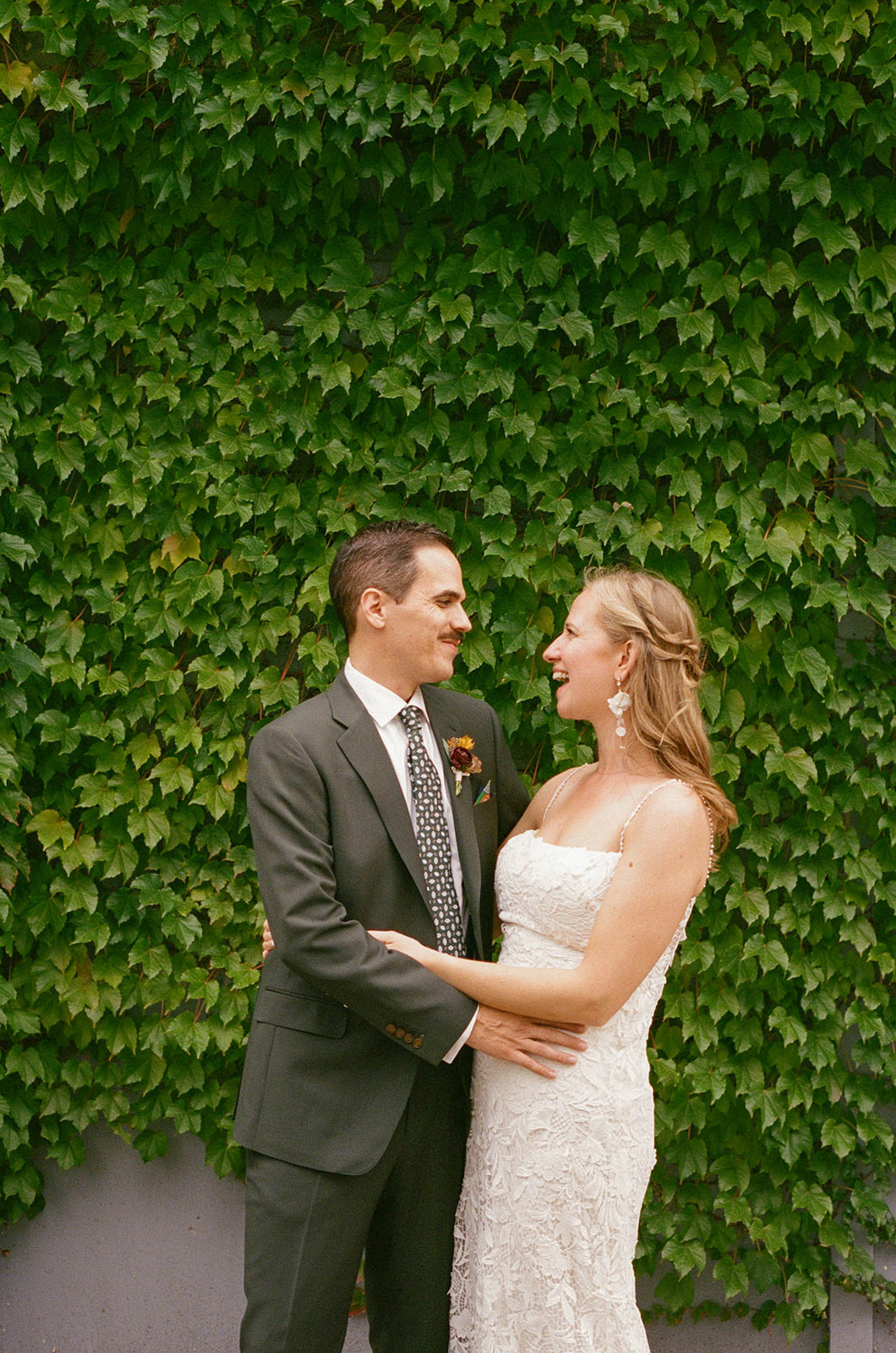 A bride and groom smile at each other outside a vine-covered wedding venue in Milwaukee.