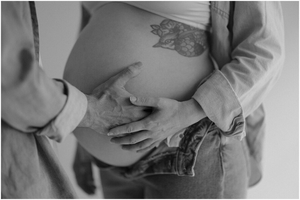 A man puts his hands on his wife's baby bump during a studio maternity session in Milwaukee.