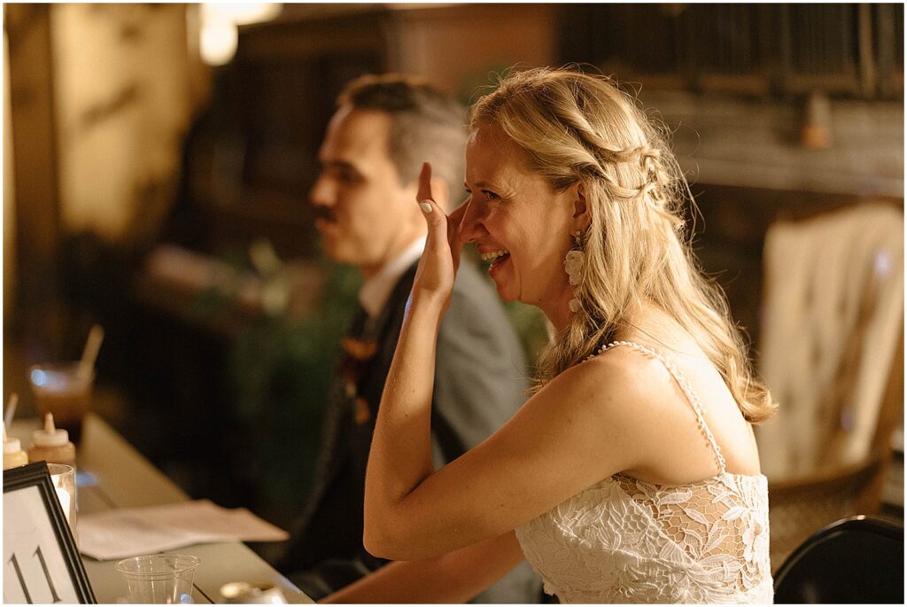 A bride laughs and wipes away a tear during a wedding toast.