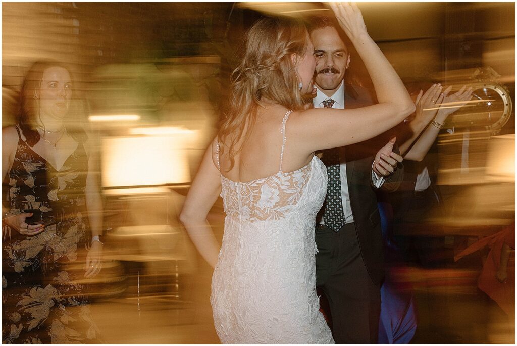 A bride and groom dance beside a floor lamp.