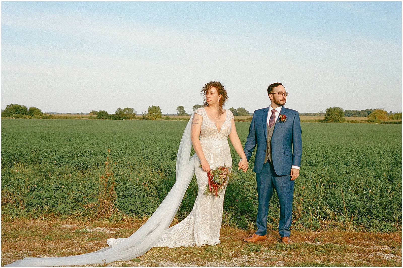 A bride and groom in a field pose for film wedding photography.