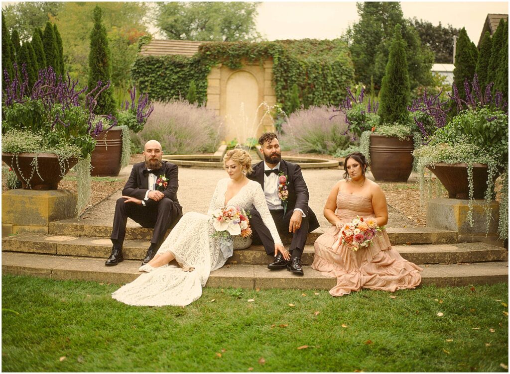 A bride and groom sit with their wedding party in a garden in film wedding photography.