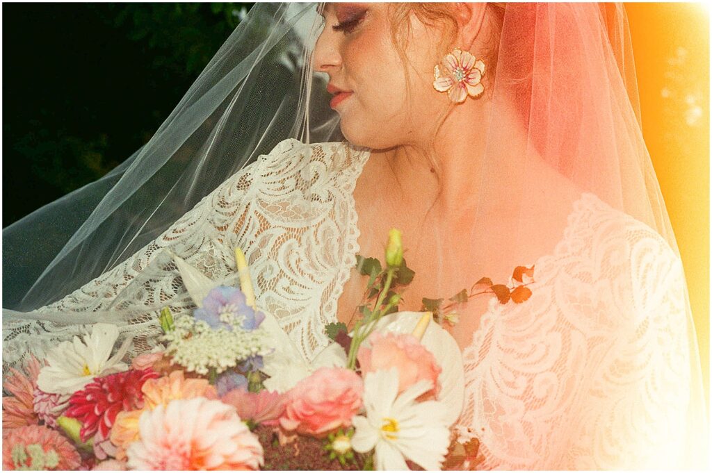 A bride holds her lace veil over her bouquet in film wedding photography.