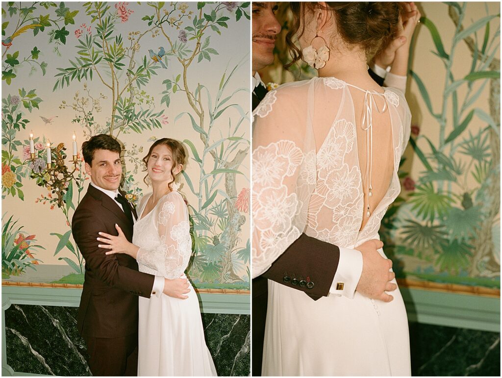 A bride and groom embrace in front of floral wallpaper in film wedding photography.