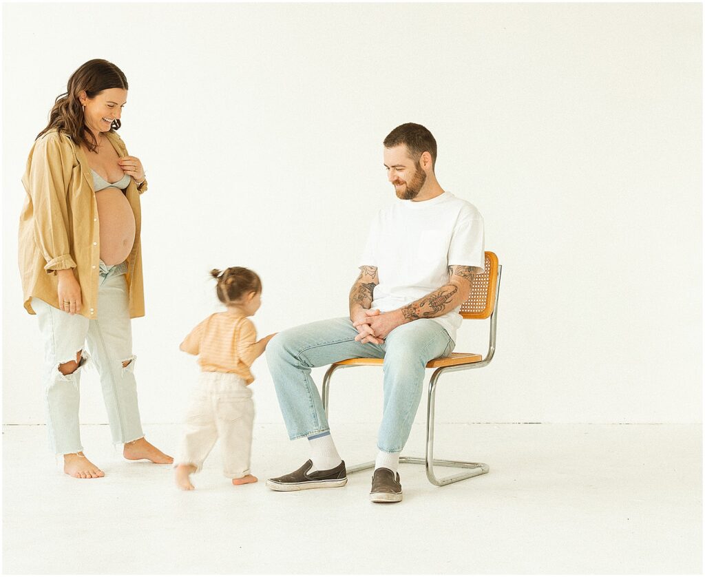 A woman and toddler walk towards a seated man in Milwaukee maternity photo.