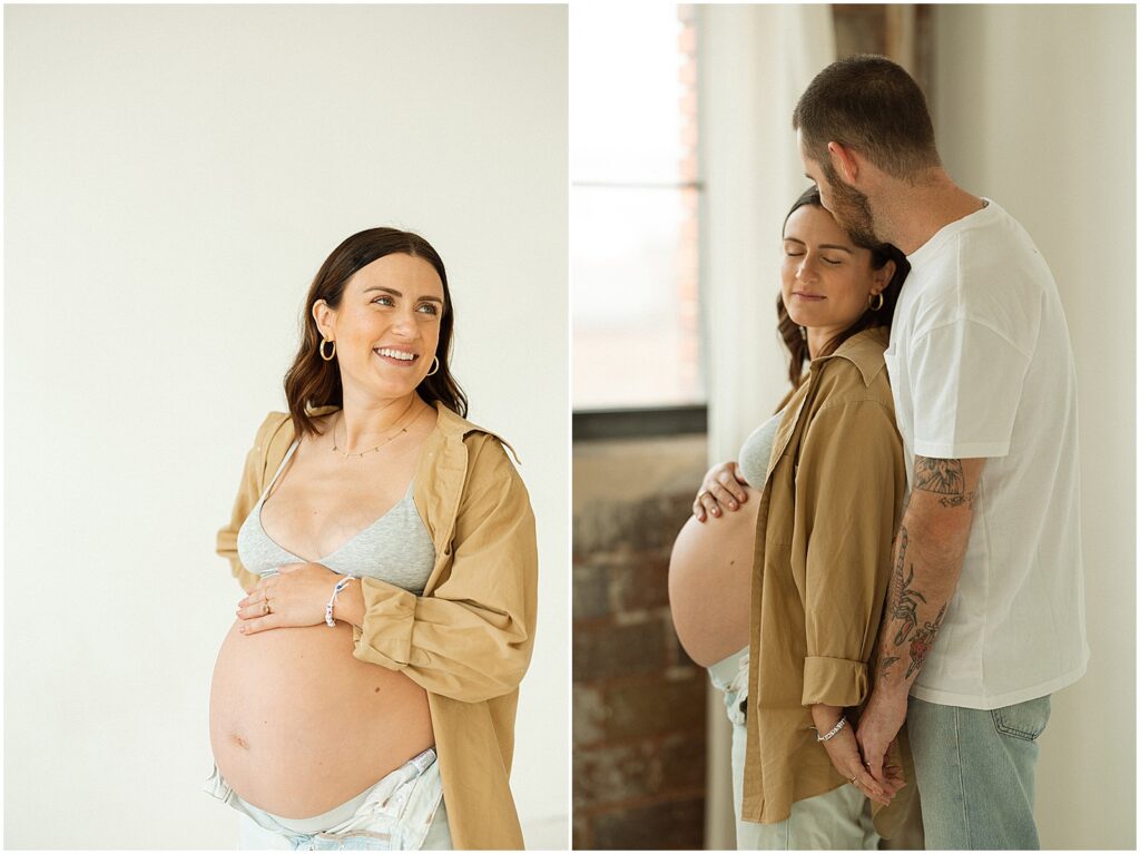 A pregnant woman and her husband hold hands beside a window in a sunlit Milwaukee photography studio.