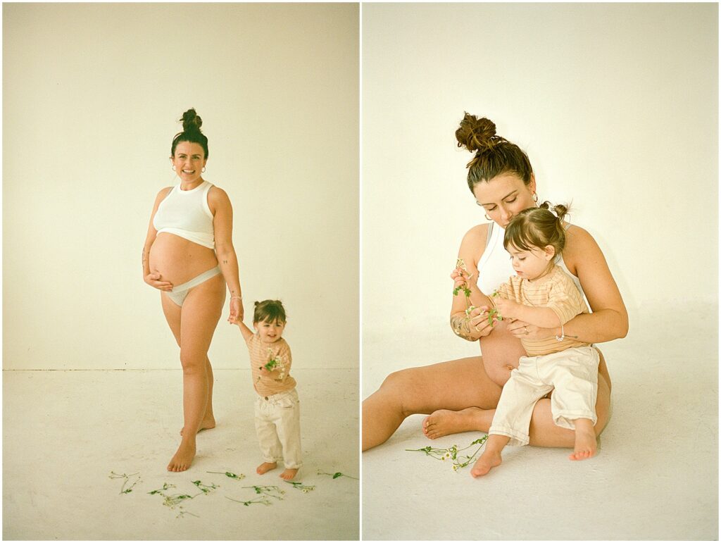 A pregnant woman holds her toddler's hand in a white Milwaukee studio for a film photography maternity session.