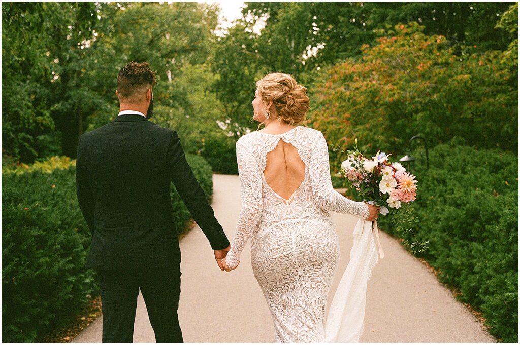 A bride and groom walk down a garden path at the Paine Art Center.