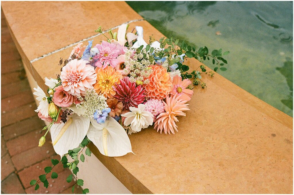 A colorful bridal bouquet sits on the edge of a fountain at a Paine Art Center wedding.