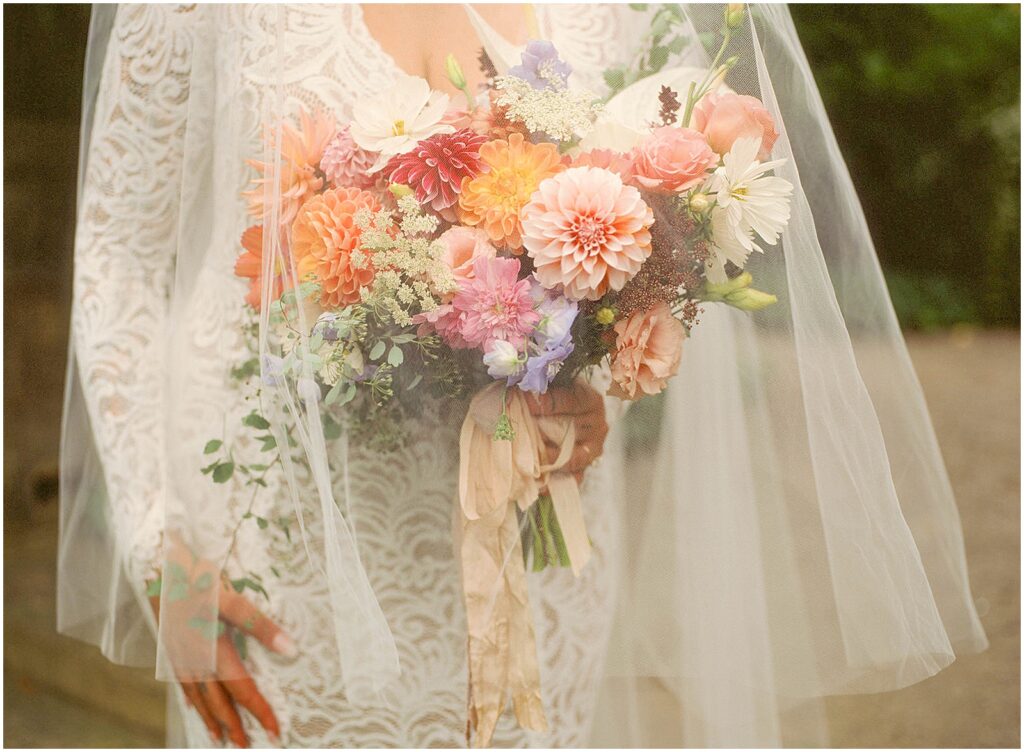 A bride holds a summer wedding bouquet under a veil.
