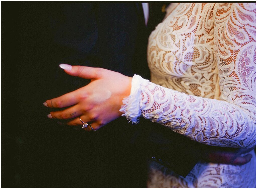 A bride's hand rests on a groom's arm in a film photo.