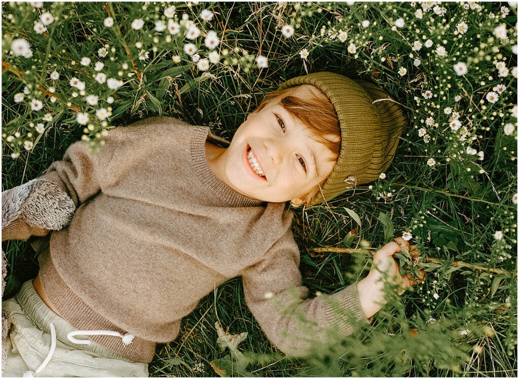 A child lays in a field of wildflowers smiling at a Milwaukee family photographer.