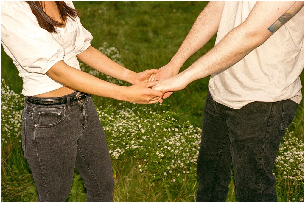 A man and woman hold hands in a field with wildflowers behind them.