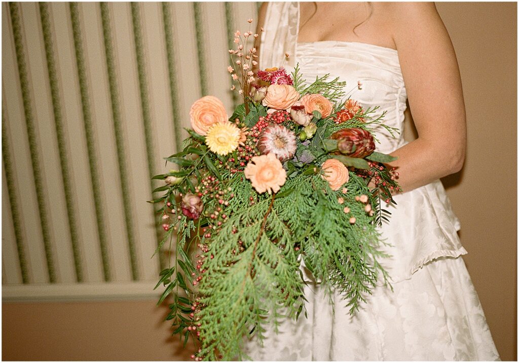 A bride holds a winter wedding bouquet of ferns and roses.