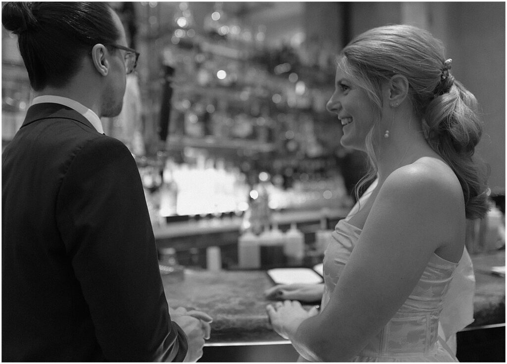 A bride and groom lean against a bar.