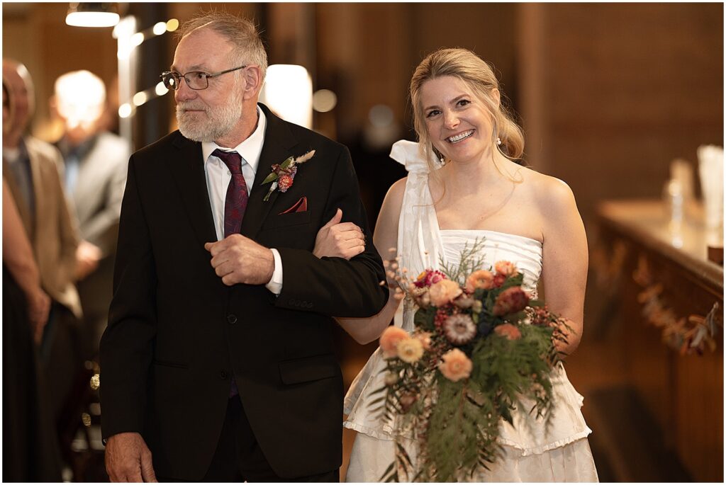 A bride's father walks her down the aisle at her Anodyne Coffee wedding.