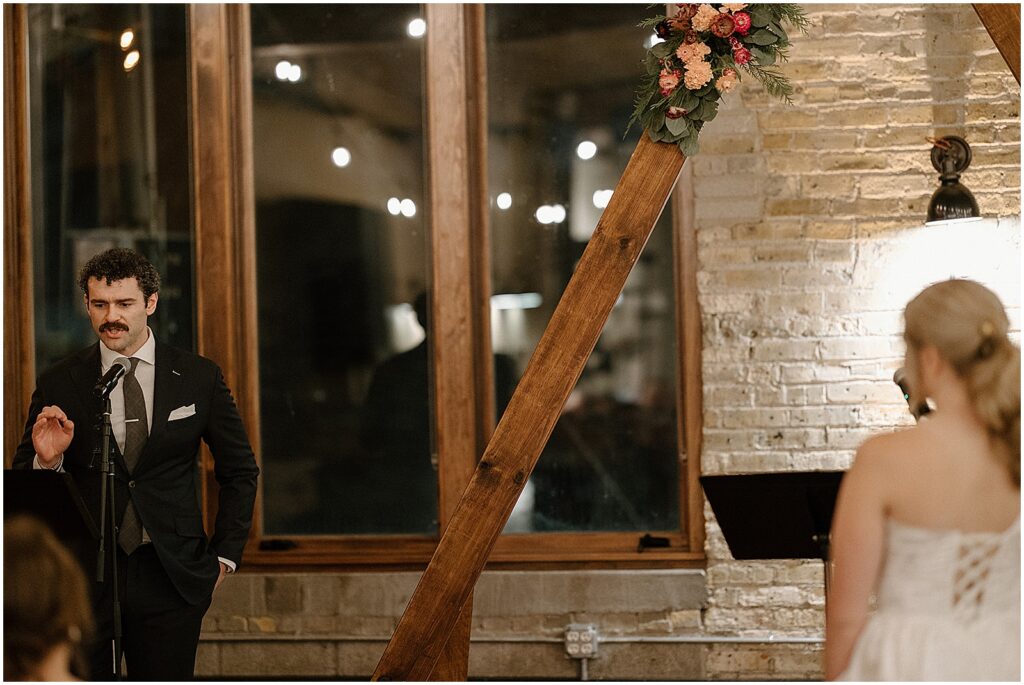 A bride watches a groom read his vows during their Anodyne Coffee wedding ceremony.