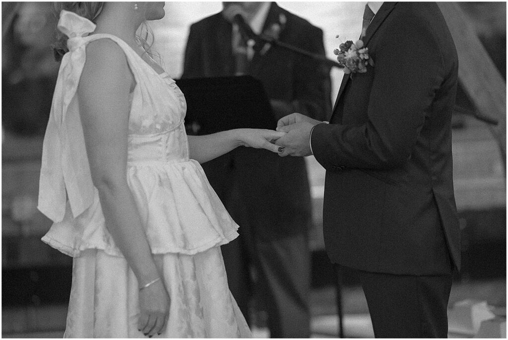 A groom puts a ring on a bride's finger.