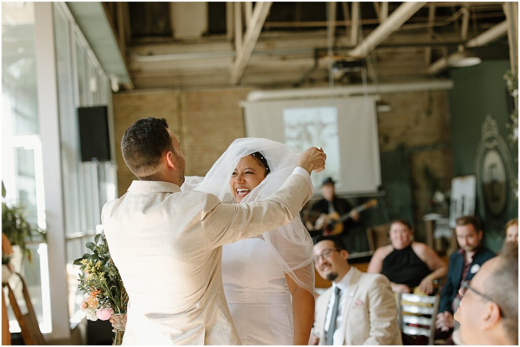 A bride's friend lifts her veil while she laughs.