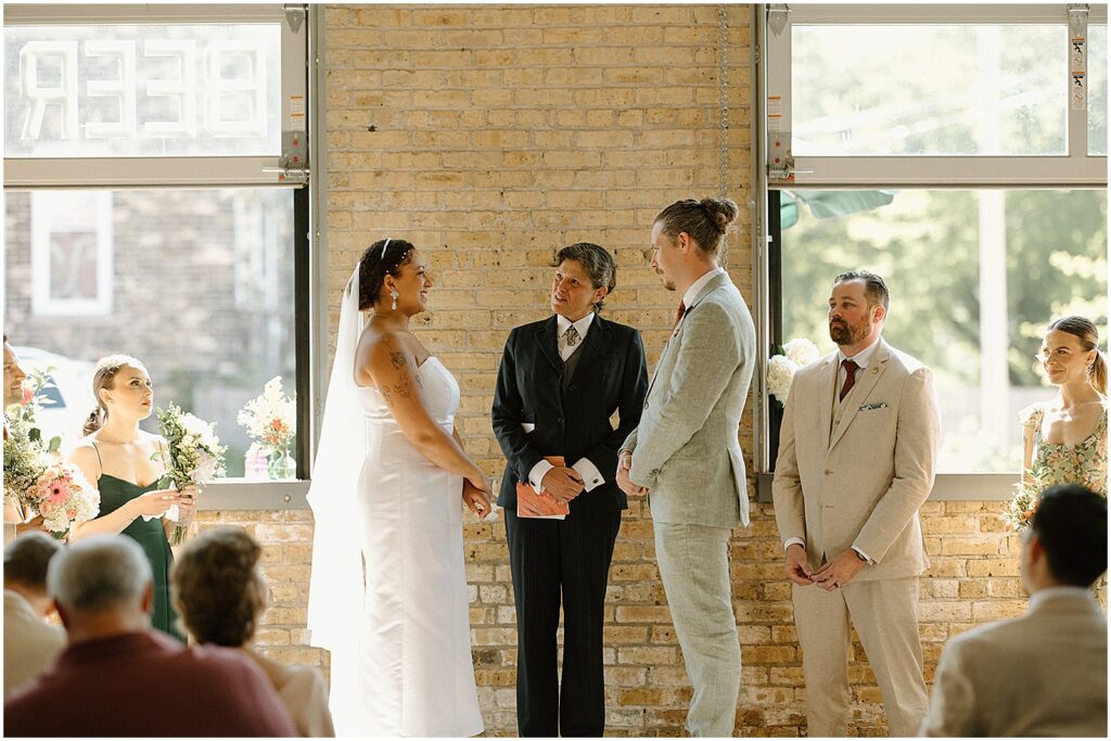 A wedding officiant speaks to a bride and groom during an Enlightened Brewing Company wedding.