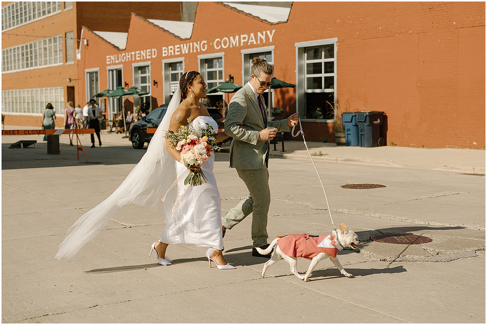 A bride and groom walk their dog past Enlightened Brewing Company on their wedding day.