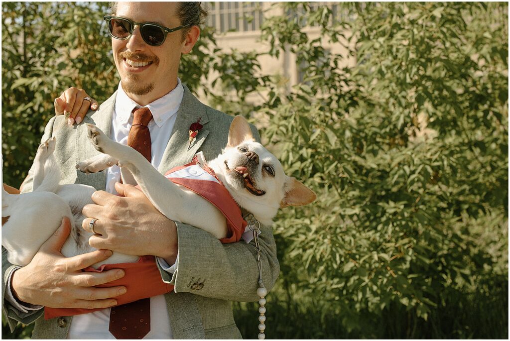 A groom laughs and cuddles a small dog.