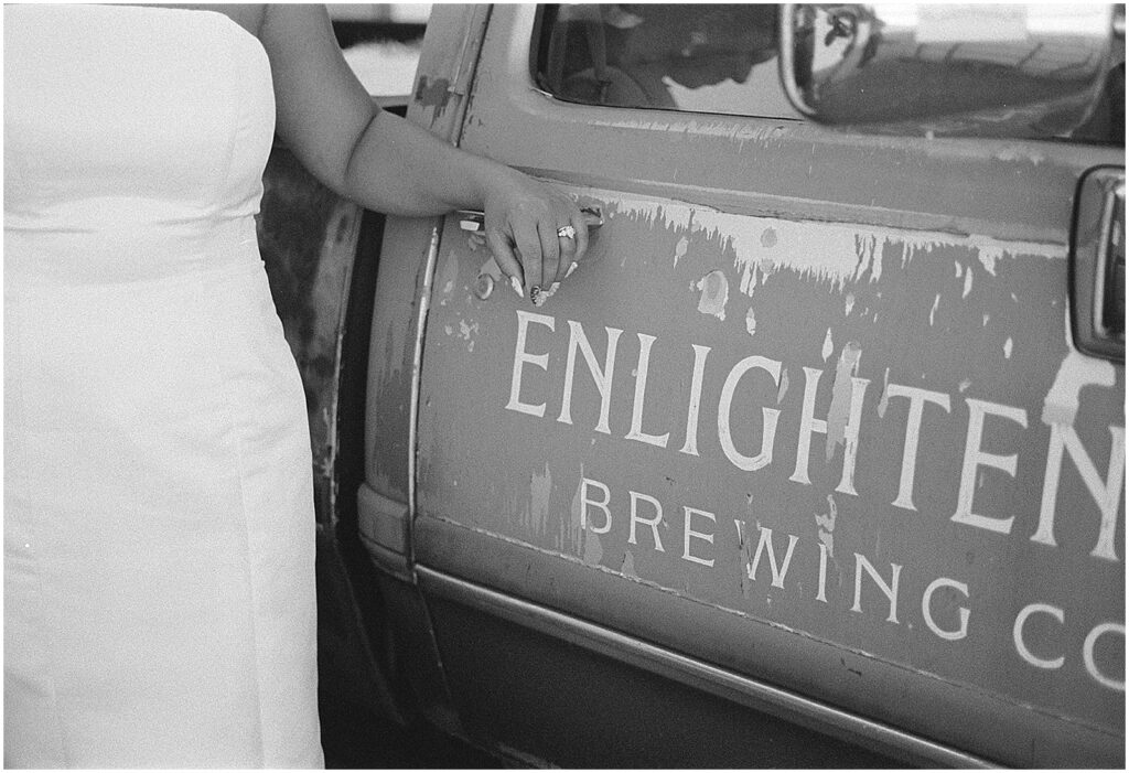 A bride leans an arm on a vintage truck outside Enlightened Brewing Company.