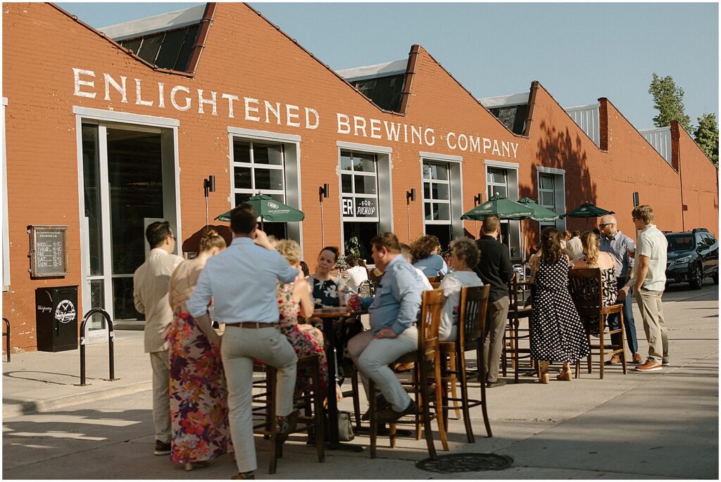 Wedding guests sit at cocktail tables on the sidewalk in front of Enlightened Brewing Company.