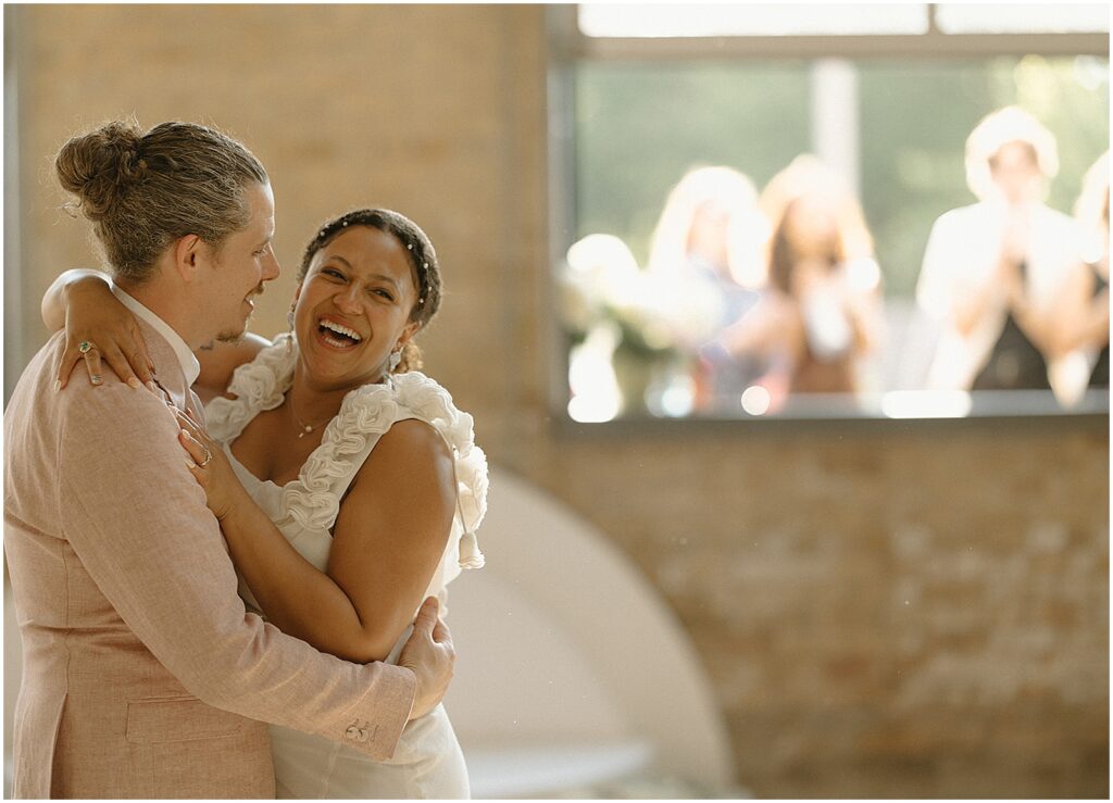 A bride laughs while she dances with a groom inside Enlightened Brewing Company.